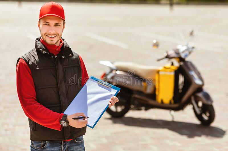 35641330786320delivery-man-uniform-holding-folder-standing-near-motorbike-outdoor-courier-career-delivery-man-uniform-holding-folder-188381090.jpg